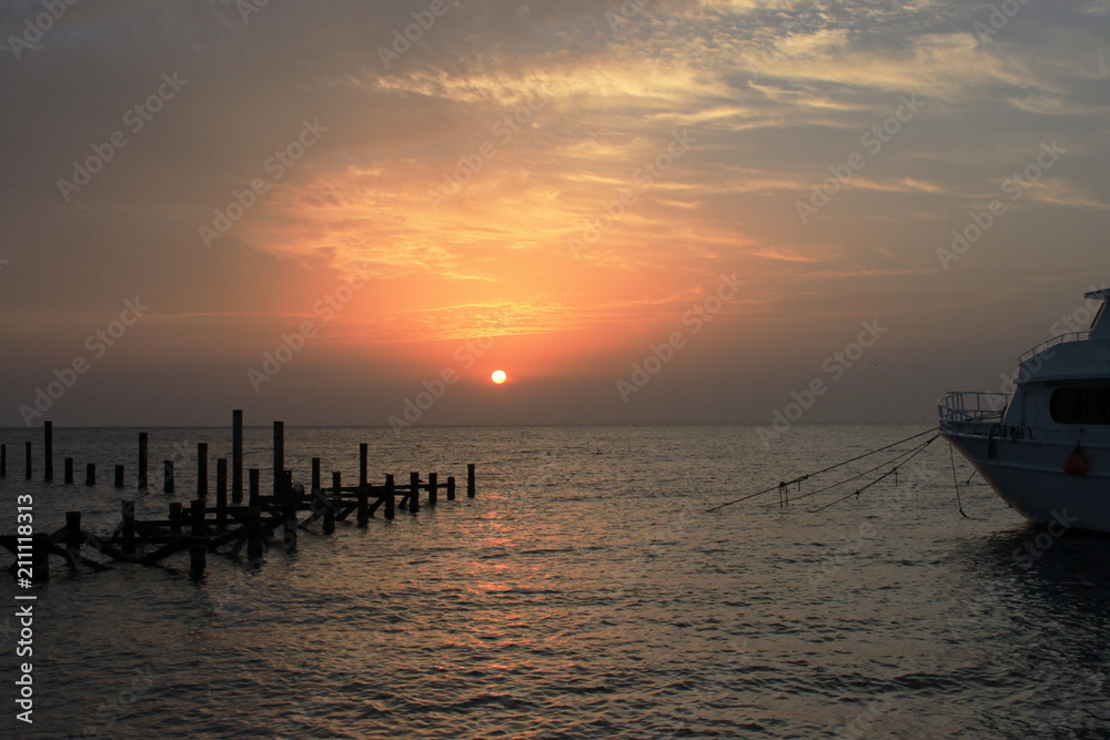 Beautiful sunset on the sea. Wooden piles of destroyed pier sticking out of the water and boat.