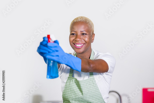 young beautiful and happy black afro american woman using detergent spray bottle as gun smiling playful cleaning and washing home kitchen isolated