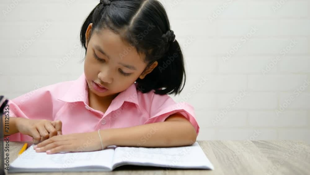 Children use a eraser is deleting words. Close up the little girl is doing homework on the wooden table.