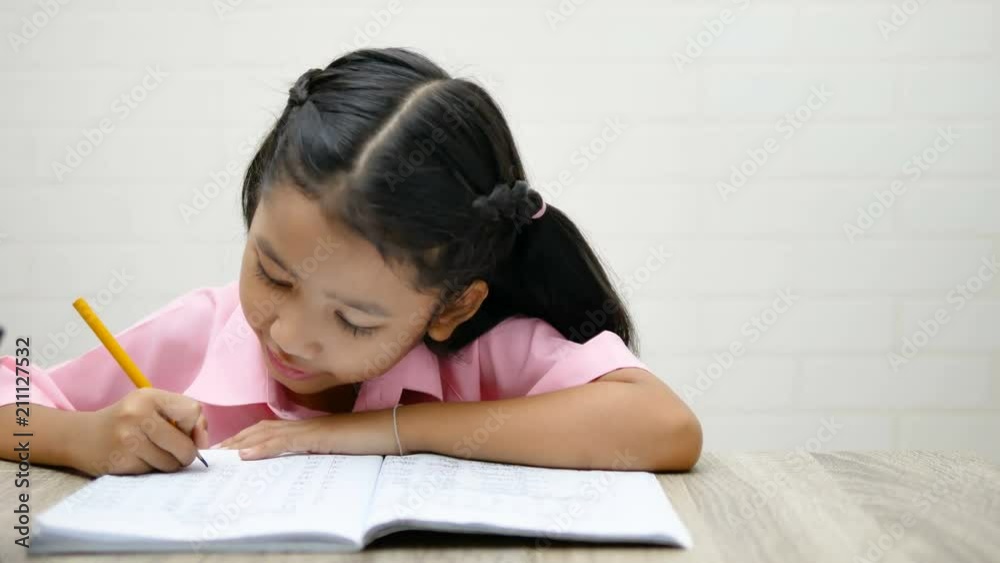 the little girl is doing homework happily. Children use a yellow pencil is writing a notebook on the wooden table. the little girl is doing homework happily. Children use a yellow pencil is writing a notebook on the wooden table.