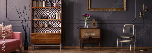 Gold chair standing in dark grey room interior with two vintage wooden cupboards with decor, books and fresh tulips photo