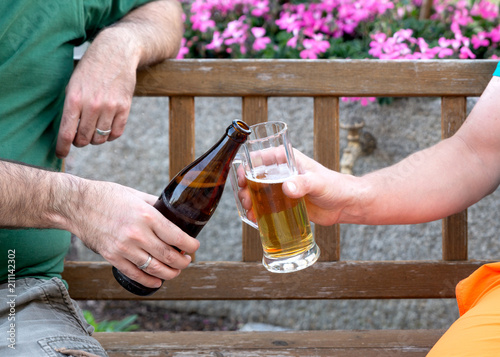 2 Männer stoßen mit Bier im Garten an photo