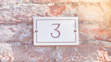 Rectangle house number plate 3 (three) on an old red brick wall