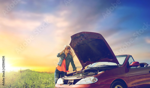 road trip, transport, travel and people concept - young woman with open hood of broken car at countryside over evening sky background photo