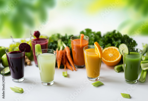 healthy eating, drinks, diet and detox concept - glasses with different fruit or vegetable juices and food on table over green natural background