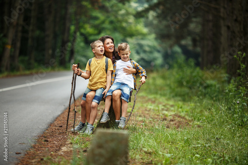 Mother and her little sons  hiking .They taking a break and sitting on rock by the road.