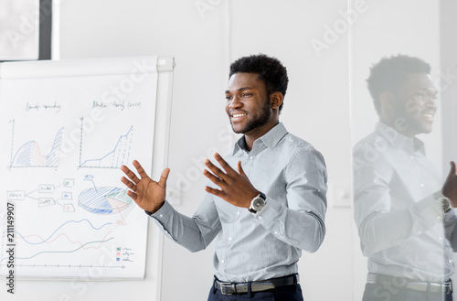 business, education and people concept - african american businessman with flip chart at office presentation