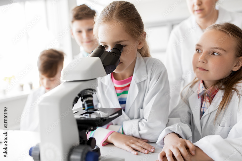 Fototapeta premium education, science and children concept - kids or students with microscope studying biology at school laboratory