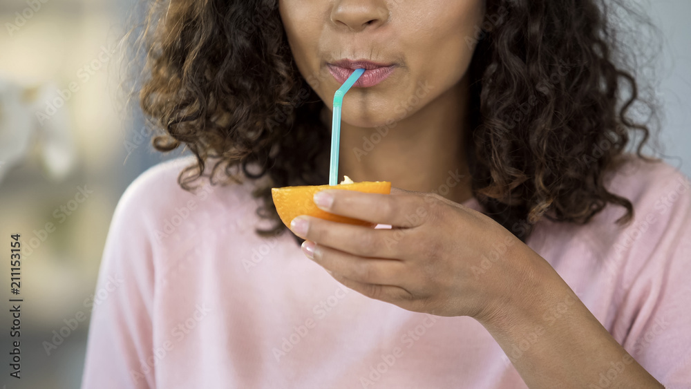 Multiracial woman drinking juice from orange half straw, health care nutrition Multiracial woman drinking juice from orange half straw, health care nutrition