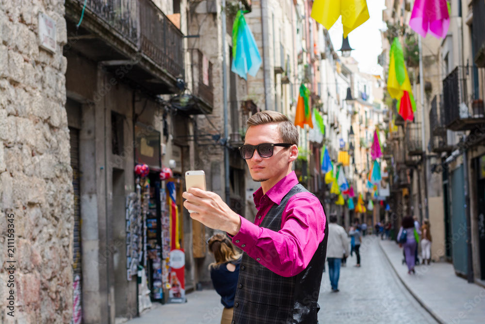 A young guy, a tourist does selfie on a mobile in the street Girona, decorated with colorful shawls, a trip to Spain