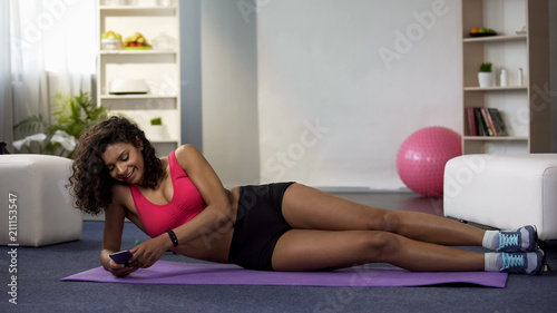 Mixed race female lying on floor in sportswear, using phone, procrastination