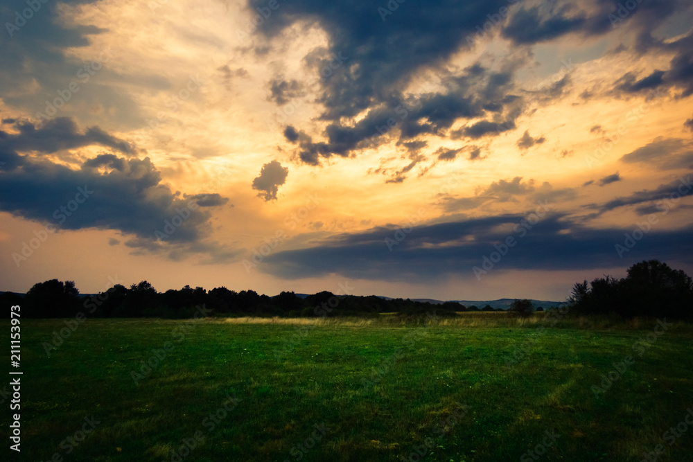Sunset with clouds over the green grass field landscape