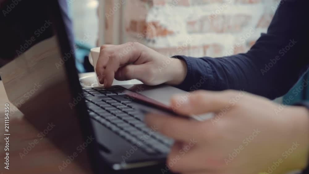 The man's hand dials credit card numbers on the computer keyboard while sitting in a cafe The man's hand dials credit card numbers on the computer keyboard while sitting in a cafe