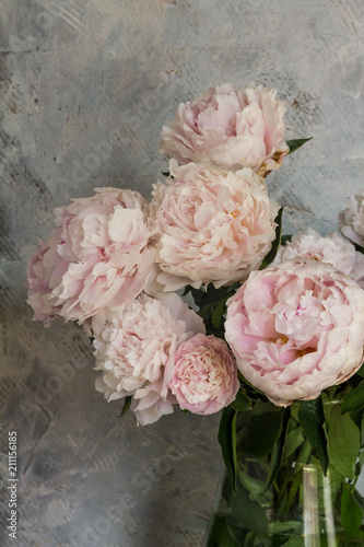 Light rose peonies in glass vase. Gray background, woodden table.