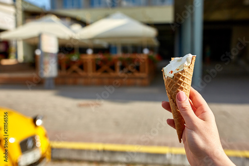 A first person view, a person walking along the road with an ice cream in his hands, shallow depth of field.