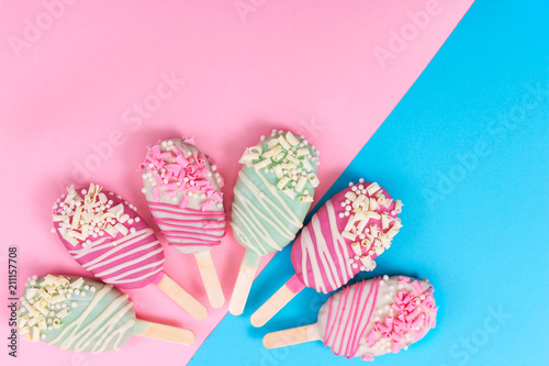 Different cake pops in form of popsicle on stick on pink and blue background.