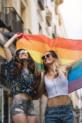 Couple lesbian woman with gay pride flag on the street of Madrid city