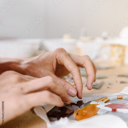 Female hands making colorful glass mosaic on table