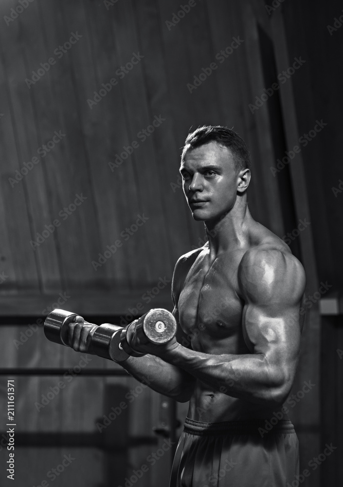 Portrait of fit young muscular man working with dumbbells, black and white image