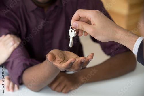 Realtor giving keys to new apartment to African American husband buyer, couple purchasing house together, black boyfriend becoming owner of first shared property with girlfriend. Ownership concept