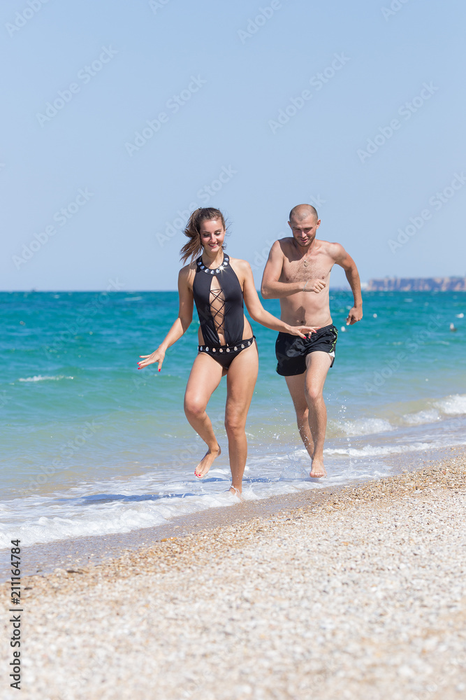 Attractive couple in swimwear running along seashore