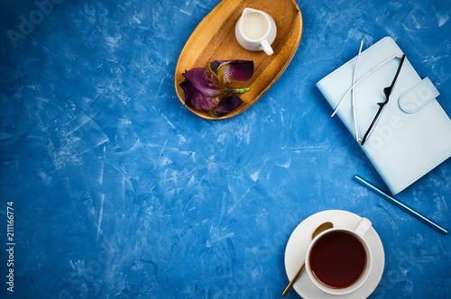 Stylish business flatlay mockup with cup of black tea, planner with glasses and pen, milk holder on wooden tray on blue cement background with copyspace