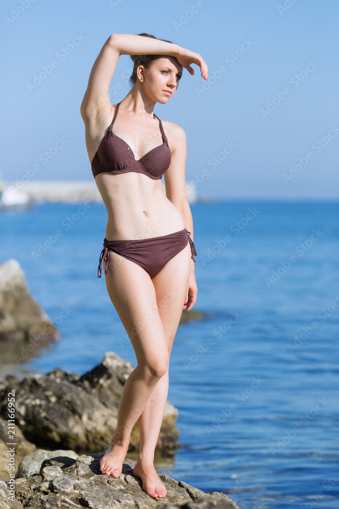 Beautiful young woman in brown bikini posing with arm raised Beautiful young woman in brown bikini posing with arm raised