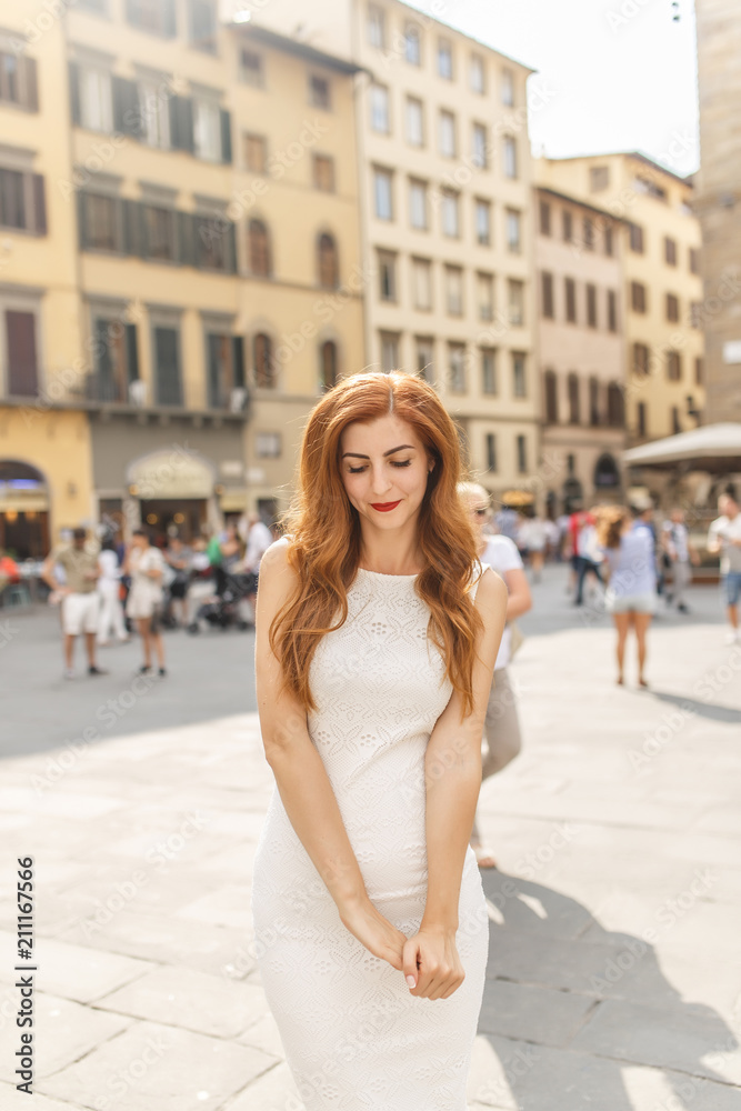 young beautiful girl with red hair and white dress is standing in Piazza della Signoria in Florence
