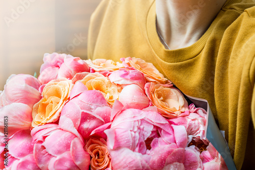 Woman is holding bunch of pink peonies and roses