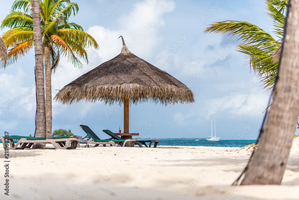 Strohschirm und Strandliegen und Getränk auf Tisch mit Palmen und Meer im Hintergrund