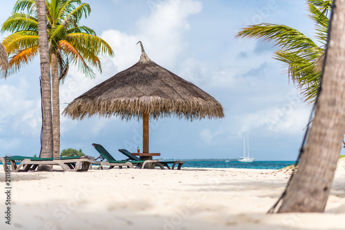 Strohschirm und Strandliegen und Getr  nk auf Tisch mit Palmen und Meer im Hintergrund