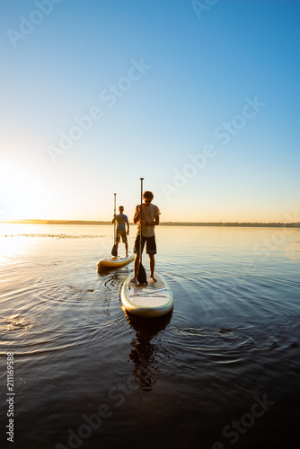 Men, friends relax on a SUP boards during sunset