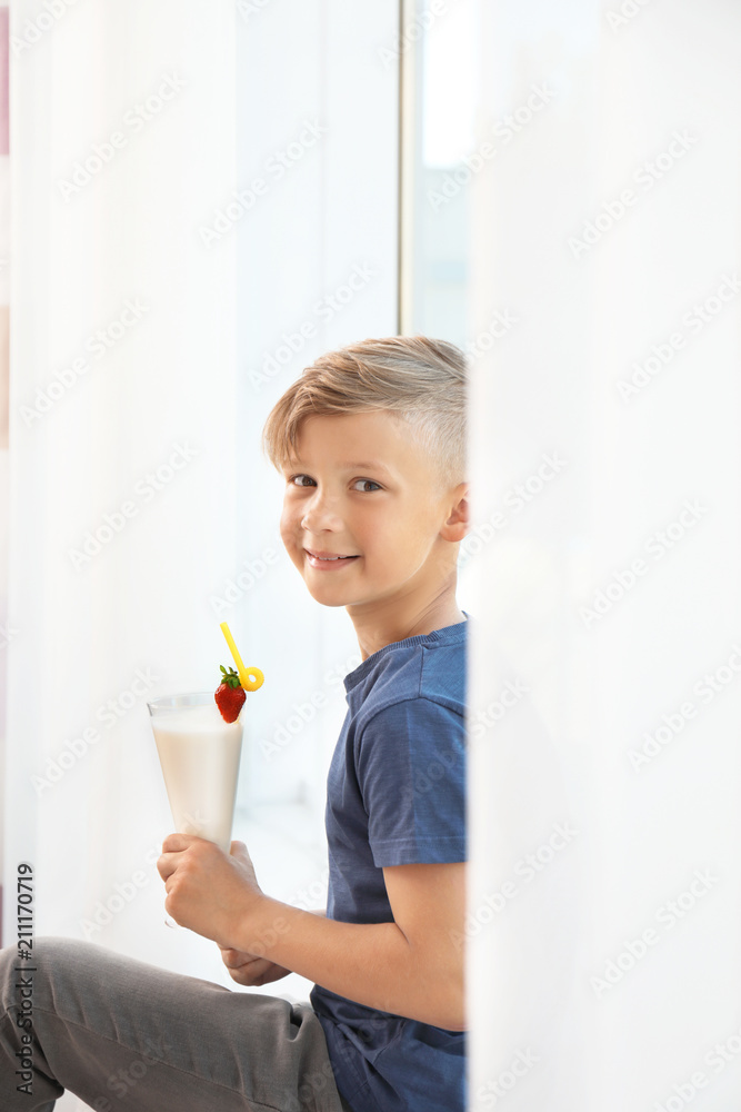 Little boy with glass of milk shake near window indoors