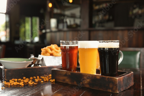 Glasses of tasty beer and snacks on wooden table in bar photo