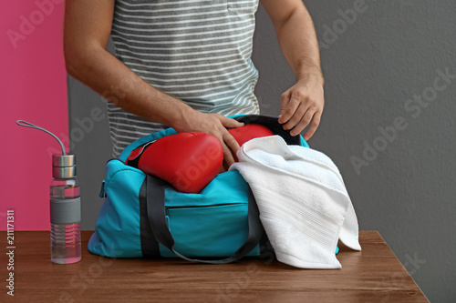 Young man packing sports bag on table