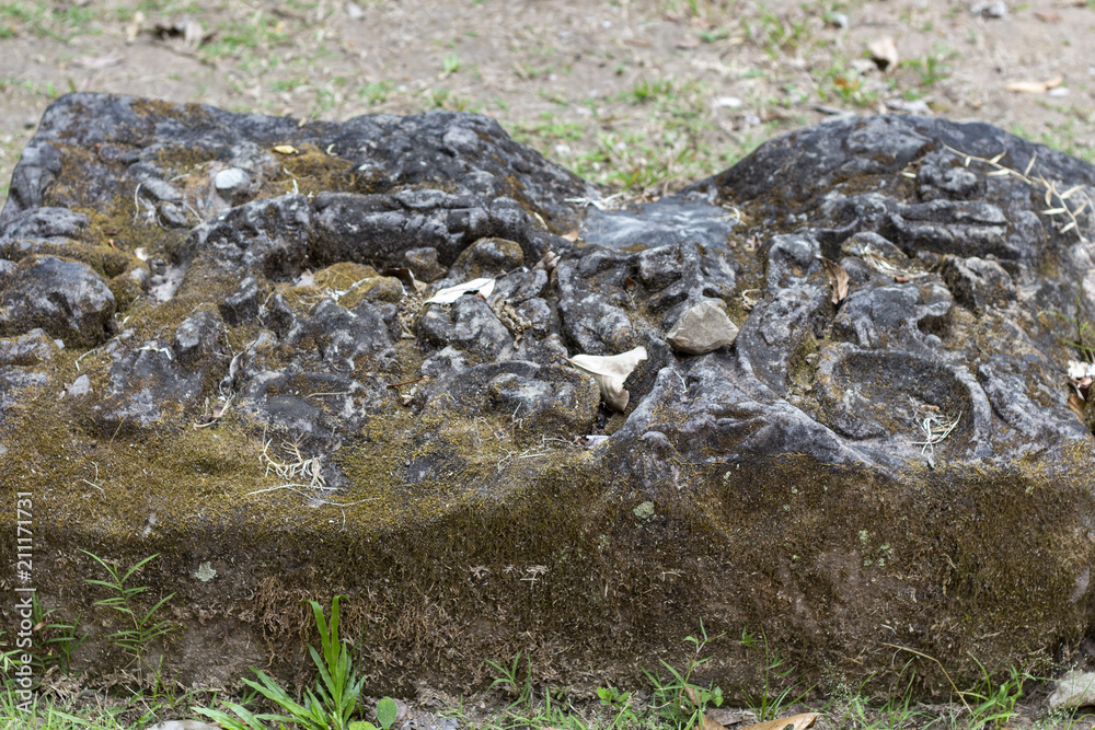 Ancient stone ruin in Angkor Wat temple. Carved stone pillar in green grass. Khmer heritage temple ruin in jungle.