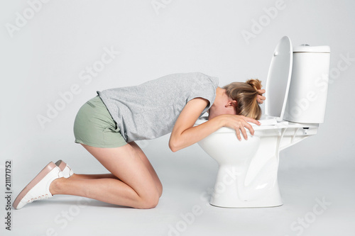 Young woman vomiting in toilet bowl on gray background photo