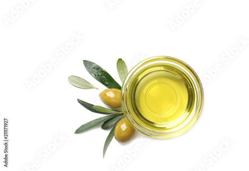 Little bowl with oil, ripe olives and leaves on white background