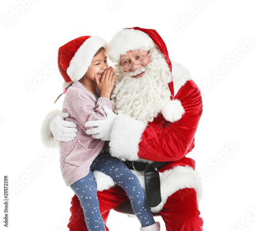 Little girl whispering in authentic Santa Claus' ear against white background