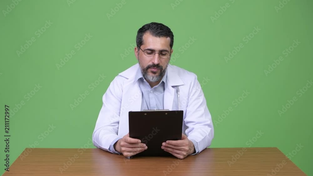 Handsome Persian bearded man doctor giving consultation while holding clipboard Handsome Persian bearded man doctor giving consultation while holding clipboard