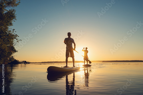 Obraz na płótnie Men, friends sail on a SUP boards in a rays of rising sun w salonie
