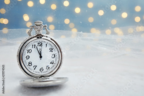 Pocket watch with snow on table against blurred lights. Christmas countdown
