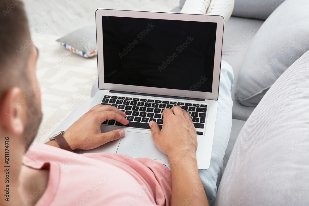 Naklejka premium Man in casual clothes using laptop on sofa at home