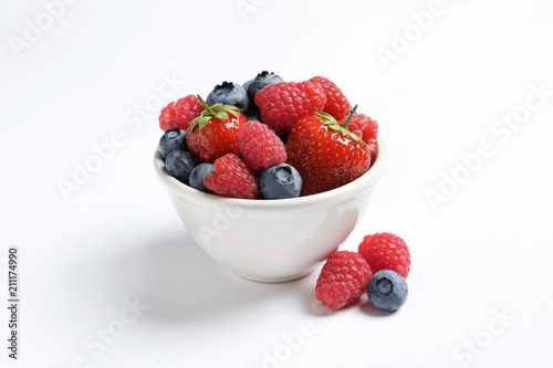 Bowl with raspberries, strawberries and blueberries on white background