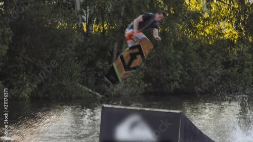 Wakeboarder ride on cable wakeboard in park, outdoor extreme slow motion on water, surfing athlete on water doing boardslide, noseslide or tailslide 180 out, backside bluntslide photo