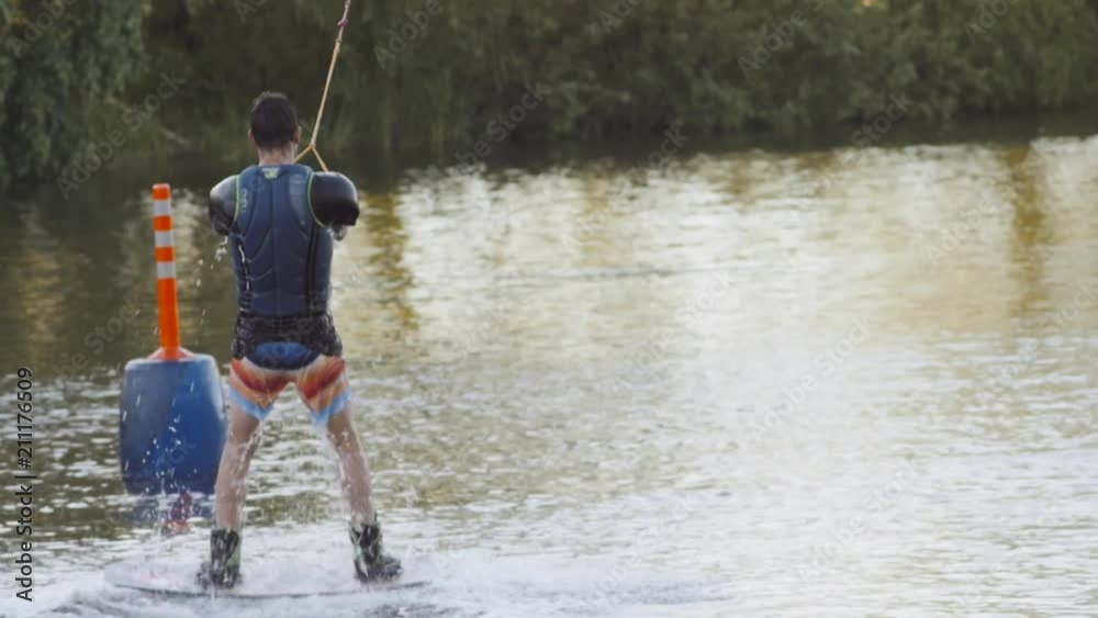 Wakeboarder ride on cable wakeboard in park, outdoor extreme slow motion on water, surfing athlete on water doing boardslide, noseslide or tailslide 180 out, backside bluntslide Wakeboarder ride on cable wakeboard in park, outdoor extreme slow motion on water, surfing athlete on water doing boardslide, noseslide or tailslide 180 out, backside bluntslide