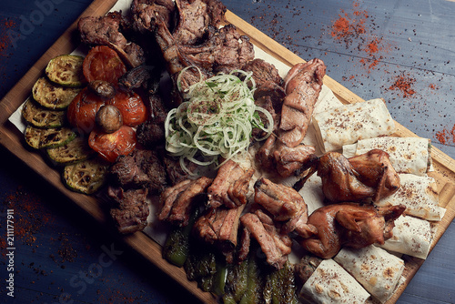 A big set of grilled meat with vegetables on big wooden plato or cutting board on gark wooden background. Tradicional georgian food. Meat like pork, beef, birds like quail. a very big set of hot meat photo
