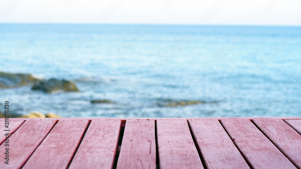 The blur cool sea background with wood floor foreground on horizon tropical sandy beach; relaxing outdoors vacation with heavenly mind view at a resort deck touching sunshine