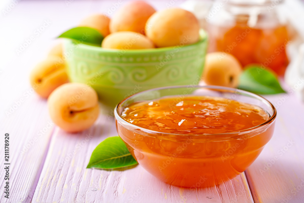 Apricot jam in glass bowl and fresh apricots on light purple wooden background Apricot jam in glass bowl and fresh apricots on light purple wooden background