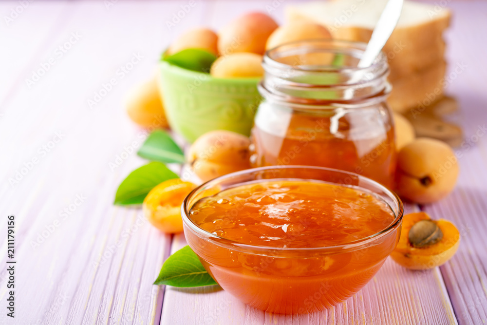 Apricot jam in glass bowl and fresh apricots on light purple wooden background Apricot jam in glass bowl and fresh apricots on light purple wooden background